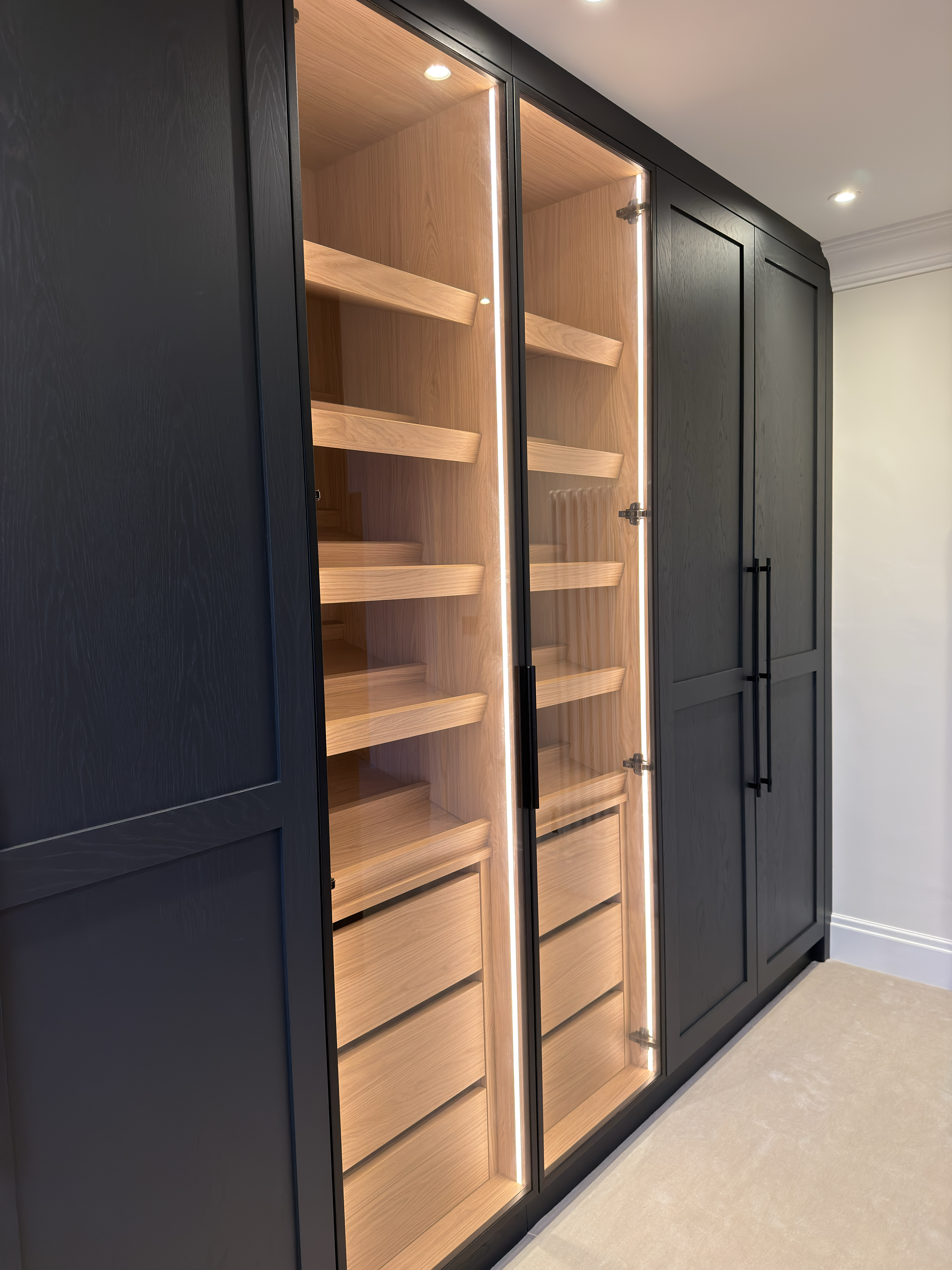 Dark bespoke fitted wardrobe with softly illuminated oak interior