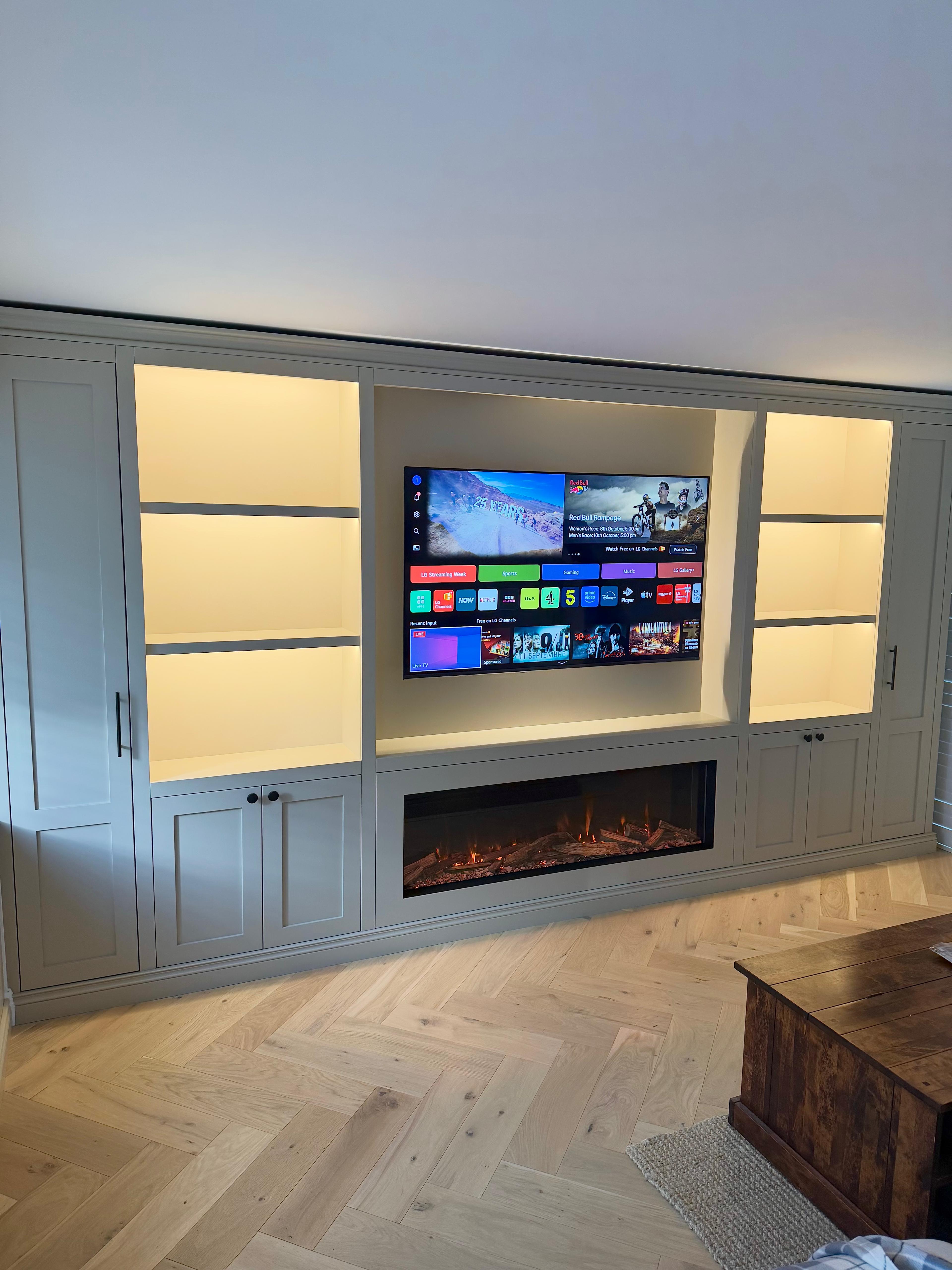 Grey bespoke media wall with illuminated shelving, integrated television and fireplace